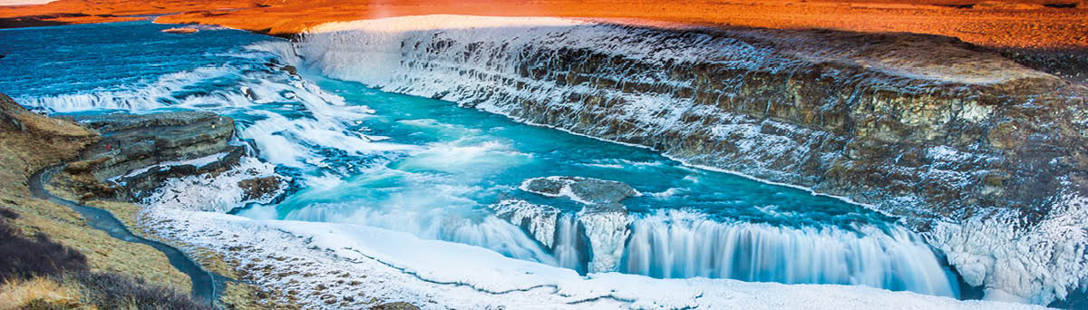 Beautiful Nordic landscape from spectacular Iceland including mighty Gullfoss waterfall partly frozen in ice as foreground and magnificent distant plane sunlit by the setting Sun for background  Very famous destination for travellers and adventurers from all over the world, this Polar country is a popular spot for tourists willing to witness and enjoy one of the wildest places in Europe  Shot with Canon EOS 60D, wide 17mm angle lens, f13, ISO 100 