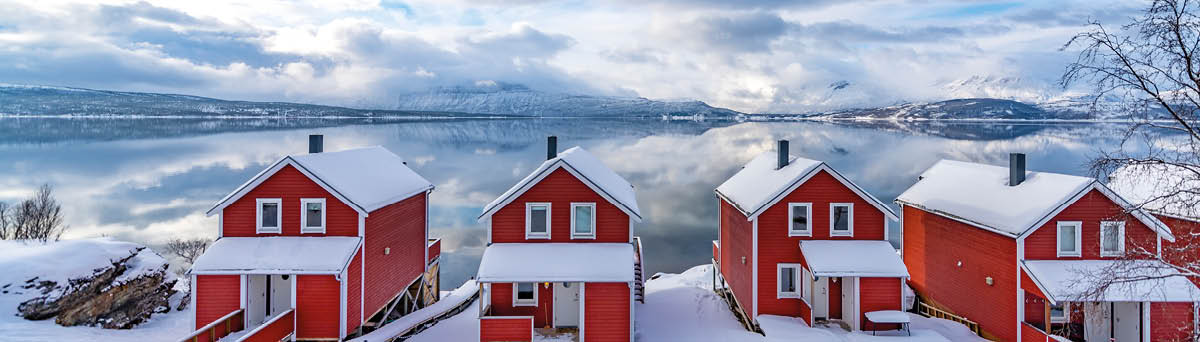 Norwegian cabin on the shore of a Fjord in Northern Norway in winter  Clouds over the Malangen fjord are bringing in new snow  The mountains in the background are reflected in the calm waters of the fjord 