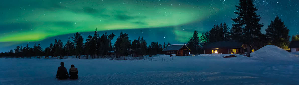 Two people sitting on the ice of a lake and watching a night sky with aurora borealis in Lapland in the north of Sweden 