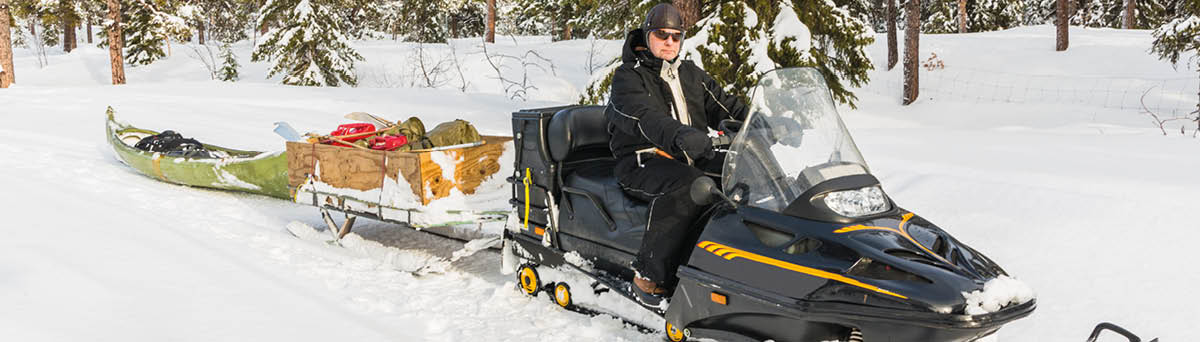 Man driving snowmobile in a forest with a canoe after the snowmobile,  GÃ llivare, Swedish Lapland, Sweden
