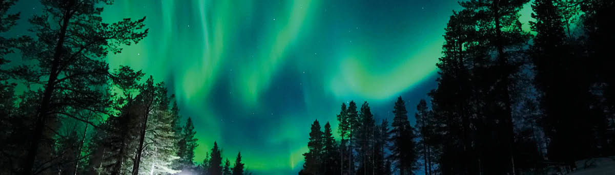 Bright lamp shining on the empty snowy road just as the northern lights appear above the idyllic Scandinavian countryside in the winter  Breathtaking aurora borealis above the calm wintry landscape 