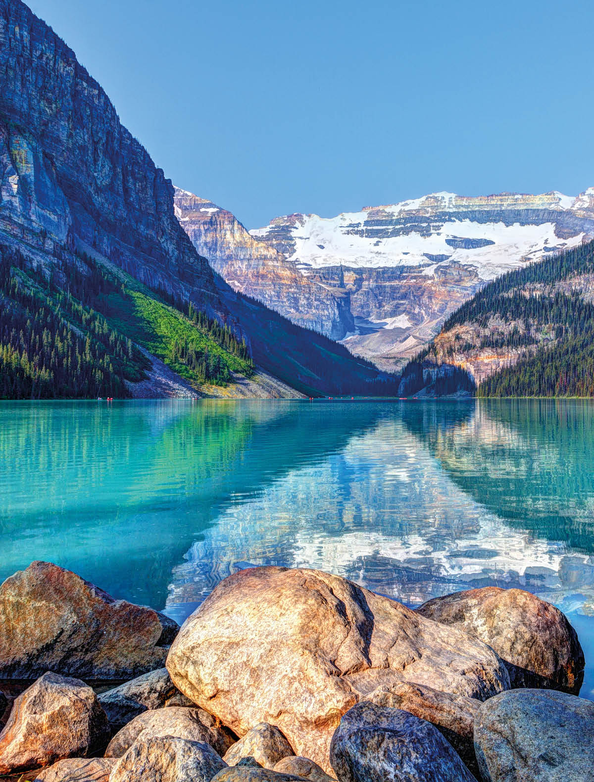 Lake Louise in Banff National Park with its glacier-fed turquoise lakes and Mount Victoria Glacier in the background. Visitors paddling red canoes in the distance.