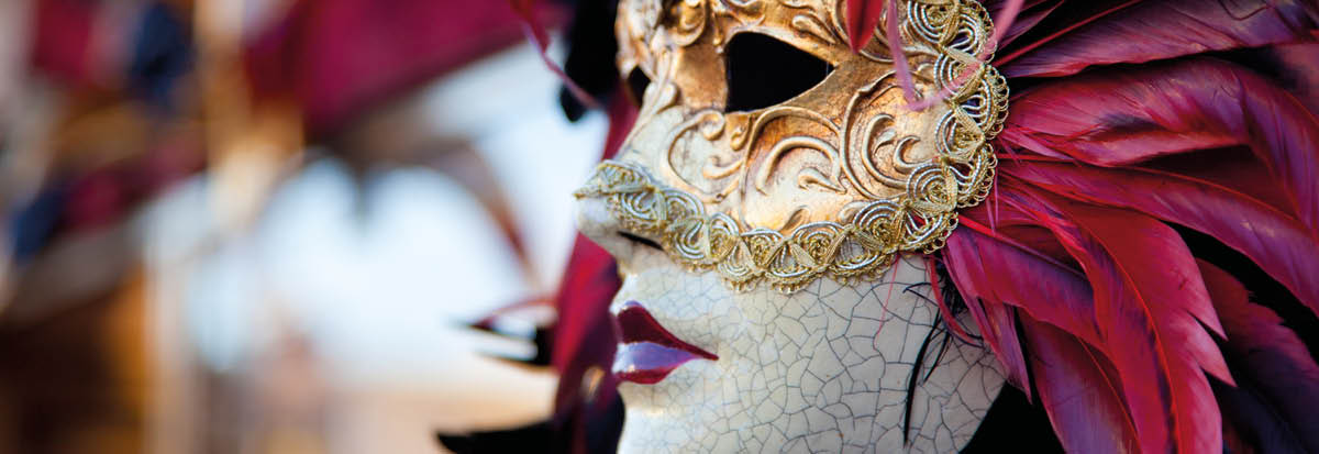 A DSLR photo of a Red Venetian Carnival mask in Venice, Italy  The mask is the main focus of the picture The mask has pink, purple and red feathers, a golden mask, a porcelain face with texture and cracks and red lips  Other blurred masks are in the background of the picture 