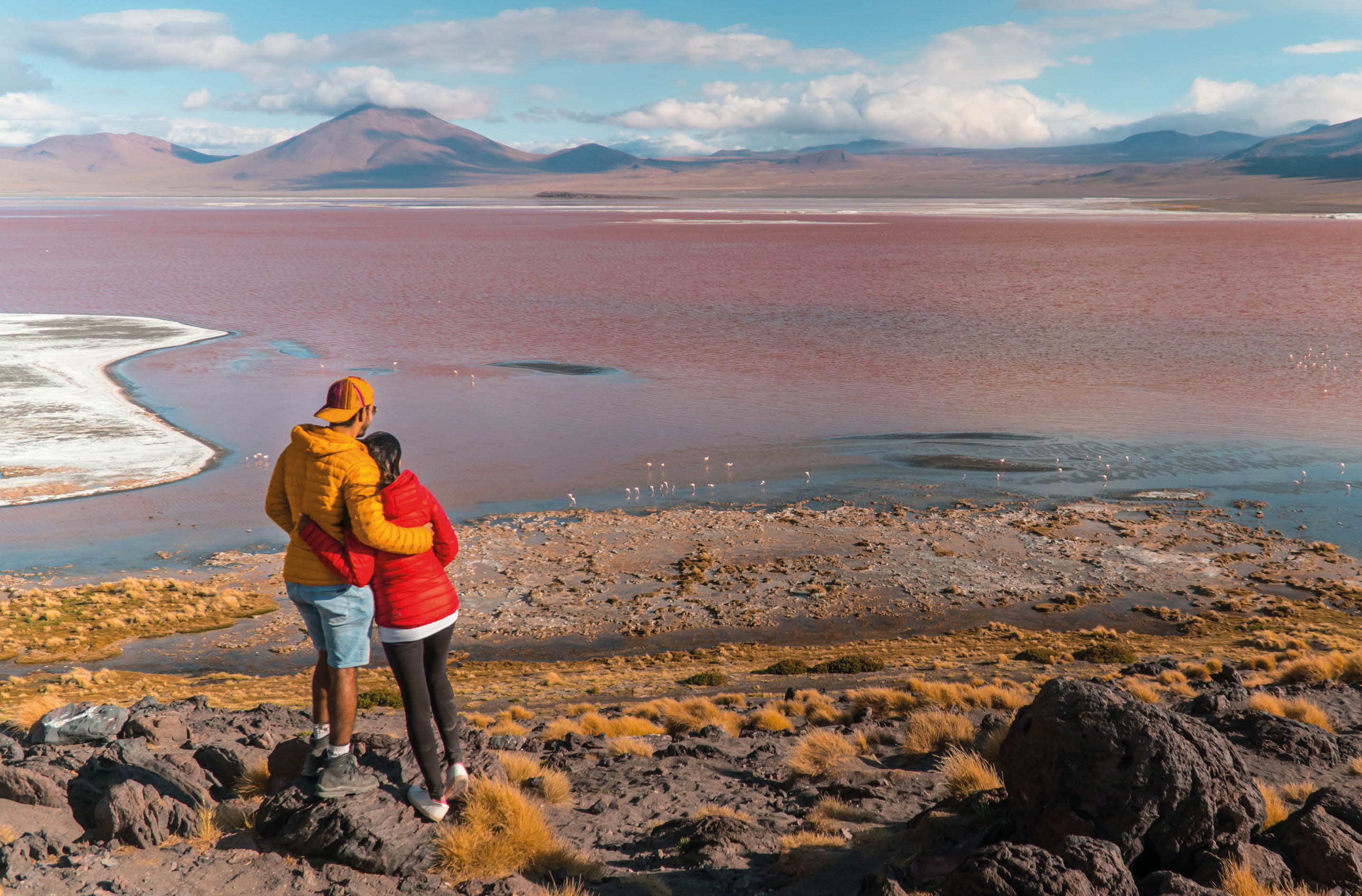 Couple with Red Lake landscape, Bolivia. Beautiful coloured water, with mountain background, and unique scenic view. Flamingos in the lake. Shot in Uyuni, Salar de Uyuni, South America. Couple in love