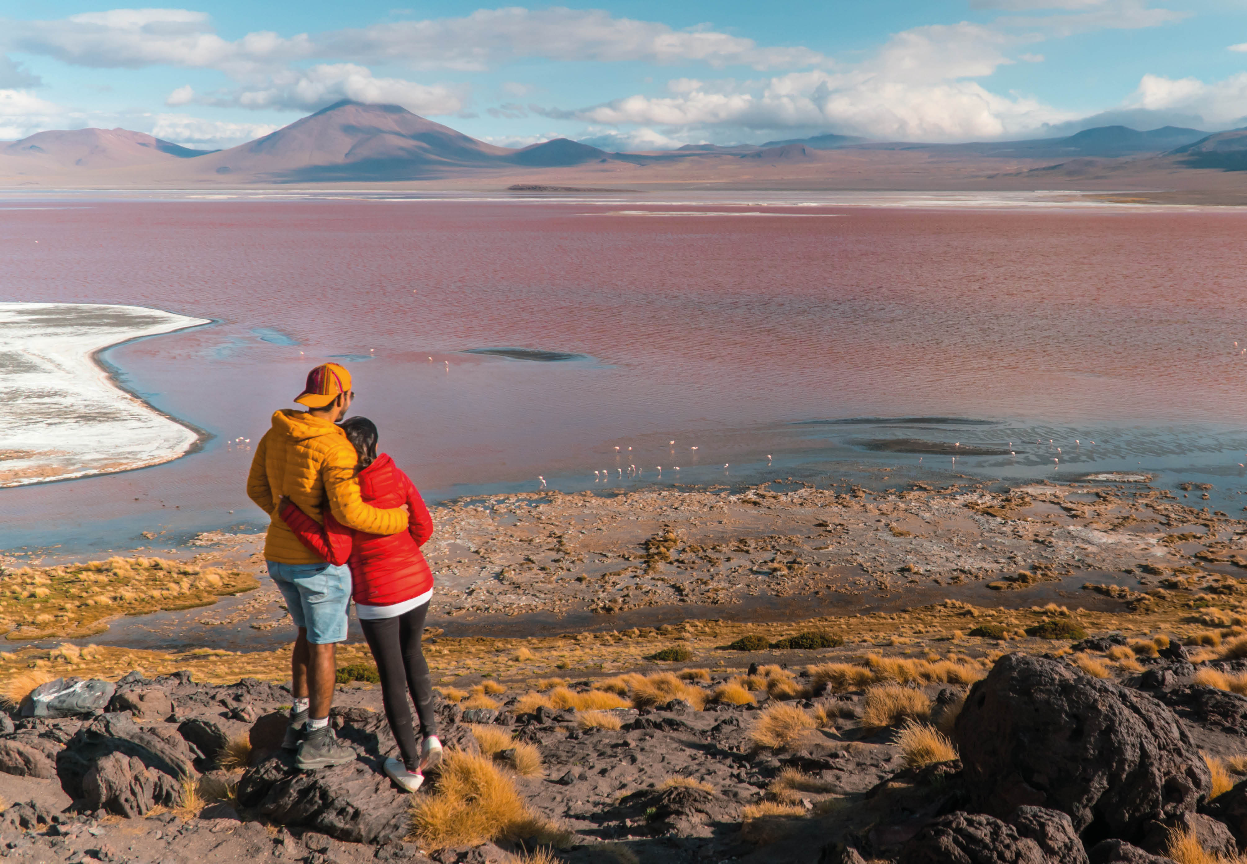 Couple with Red Lake landscape, Bolivia. Beautiful coloured water, with mountain background, and unique scenic view. Flamingos in the lake. Shot in Uyuni, Salar de Uyuni, South America. Couple in love