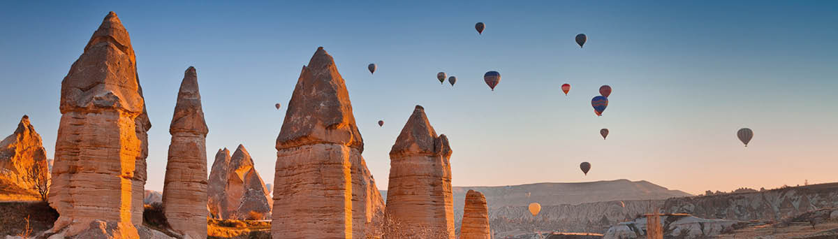 Balloons rising above the Love Valley in Cappadocia, Turkey  The sunlight is hitting the pillars at dawn, sunrise as the hot air balloons rise above the ground in the gentle still air of the morning 