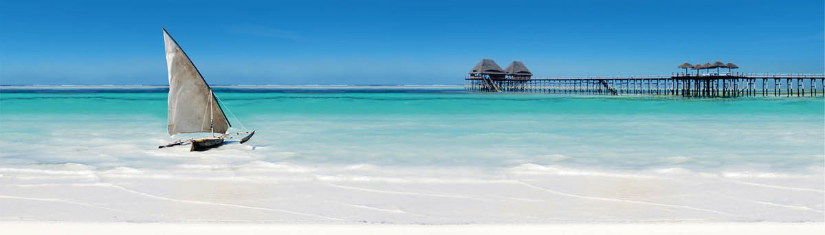 sail boat in the sea beside the white sandy beach with pier and blue skies