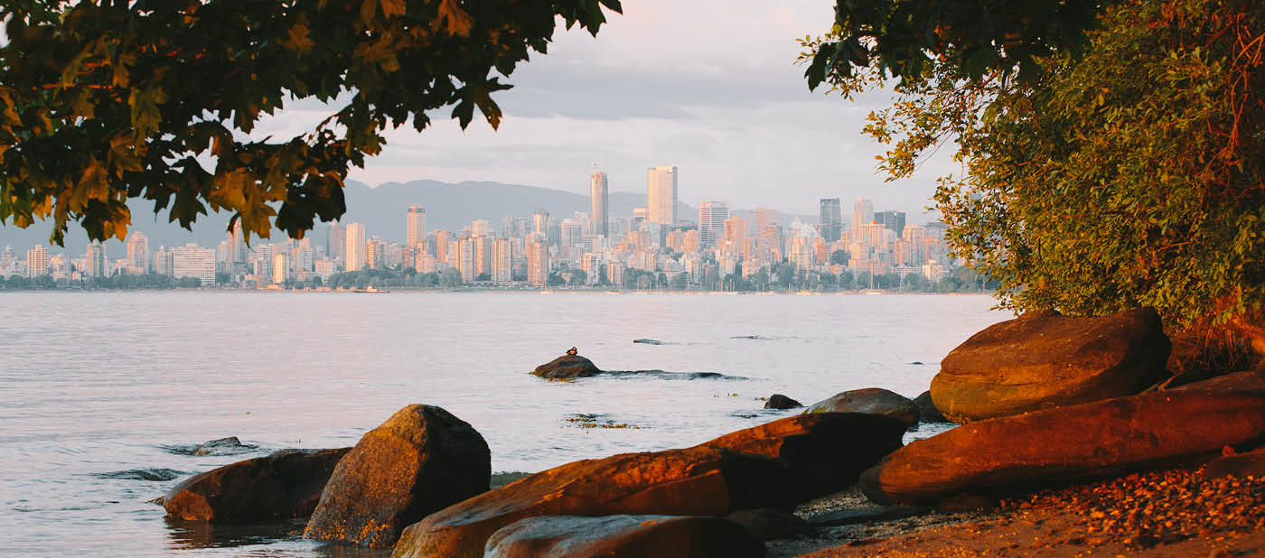 Vancouver skyline from Kitsilano. Beach with rocks and trees.