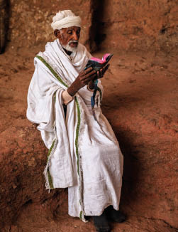 Priest of rock-hewn church reading holy book near one of Lalibela's churches, northern Ethiopia, Africa  Lalibela is famous for its rock-cut churches and is one of Ethiopia's holiest cities http:  bhphoto pl IS ethiopia_380 jpg