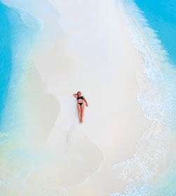 Beautiful woman tans on sandbank surrounded by turquoise ocean from above